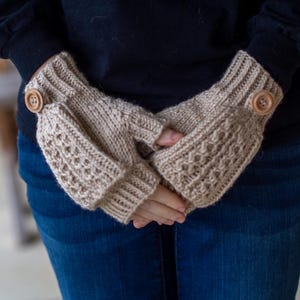 Könnte beinhalten: Beige gestrickte Fingerhandschuhe mit strukturiertem Muster und Holzknopfdetails. Die Handschuhe haben eine gerippte Manschette und ein dekoratives Muster auf der Hand. Ein gemütliches Accessoire für kühleres Wetter.