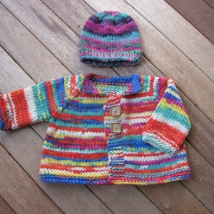 May include: A colorful striped knitted cardigan with wooden buttons. The cardigan is a bright mix of red, orange, yellow, green, blue, and white stripes. It is paired with a matching striped knit hat.