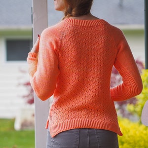 Può includere: Un maglione di maglia color corallo arancio con una vestibilità ampia e un delicato motivo traforato. Il maglione ha un collo rotondo e maniche lunghe.
