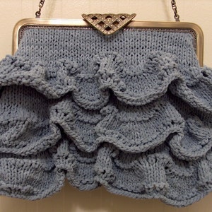 Puede incluir: Un bolso de mano de punto azul claro con un diseño de volantes y un cierre de metal plateado.