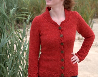 May include: A red knitted cardigan with a shawl collar and button closure. The long-sleeved sweater features decorative stitching on the cuffs and hem. The cardigan is worn with dark trousers.