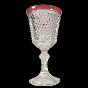 Puede incluir: Una copa de vidrio transparente con un patrón de diamante y un borde rojo. La copa tiene un tallo alto y una base ancha.