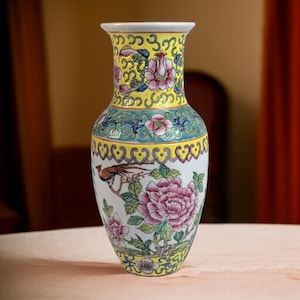 Puede incluir: Un jarrón de porcelana blanca con un diseño floral amarillo, verde y azul. El jarrón presenta un pájaro y flores en rosa, rojo y verde.