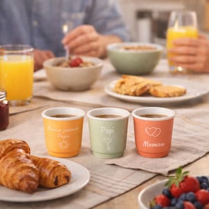 Peut inclure: Trois petites tasses à café colorées sur une table. Les tasses sont orange, vertes et corail, chacune avec une inscription différente. La tasse orange dit "Bonne journée Papa" avec un soleil. La tasse verte dit "Papi" avec une clé. La tasse corail dit "Maman" avec des coeurs.