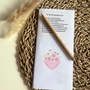 May include: A white sheet of paper with a list of items needed for daycare. The list includes: change of clothes, comfortable clothing, a pencil, and communication with teachers. The paper is on a woven straw mat with a small bouquet of pink flowers in a pink pot.