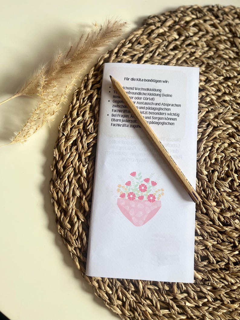 May include: A white sheet of paper with a list of items needed for daycare. The list includes: change of clothes, comfortable clothing, a pencil, and communication with teachers. The paper is on a woven straw mat with a small bouquet of pink flowers in a pink pot.