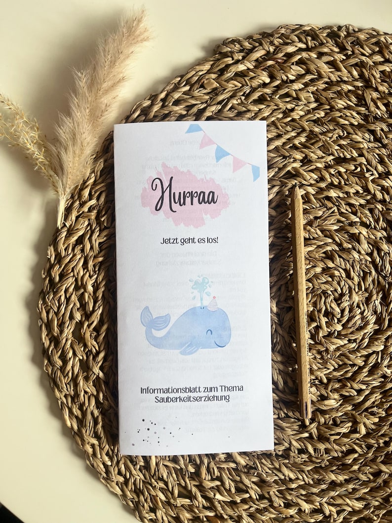May include: A light blue whale with a crown on its head is shown on a white sheet of paper with the text "Hurraa! Jetzt geht es los!" and "Informationsblatt zum Thema Sauberkeitserziehung".