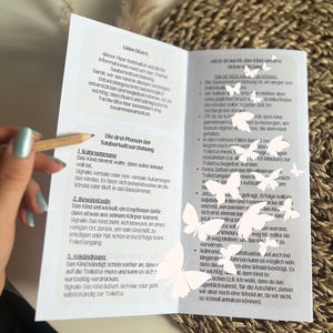 May include: A close-up of a folded pamphlet with the title "Liebe Eltern" and the text "Die drei Phasen der Sauberkeitserziehung" in German. The pamphlet provides information about potty training for children.