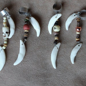 May include: Seven silver and bone finger rings with various charms and beads. The charms include skulls, beads, and other decorative elements. The rings are all different lengths and styles.