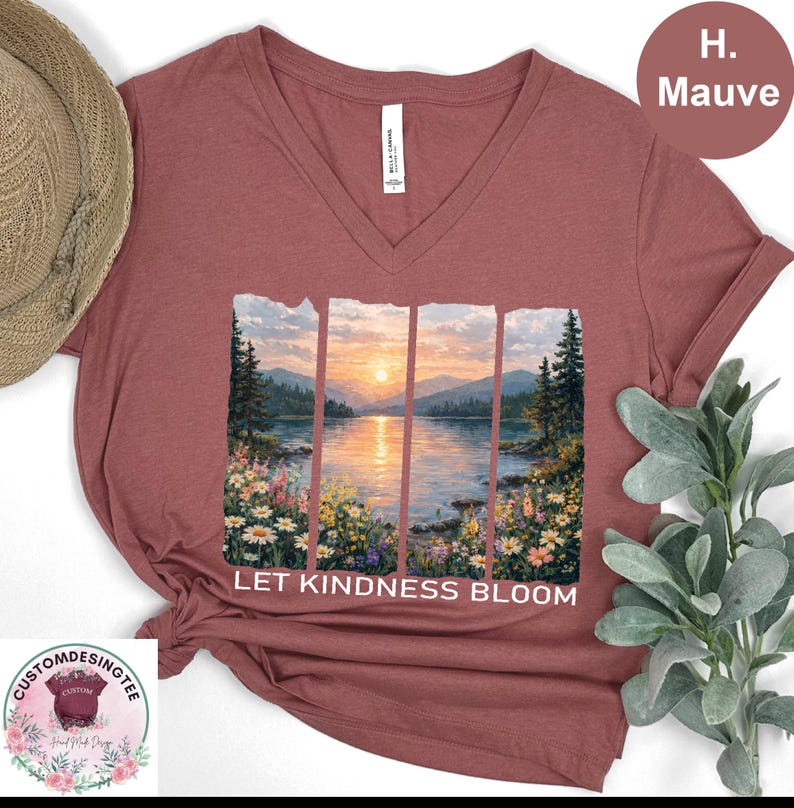 a red v-neck t-shirt with a printed design depicting a serene landscape with a lake, mountains, and a sunset. The text "LET KINDNESS BLOOM" is printed below the image.