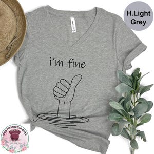 a gray t-shirt with a hand giving a thumbs up, accompanied by a straw hat and a plant.