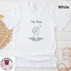 A white t-shirt with a graphic design depicting a hand giving a thumbs up, with the text "i'm fine" above the hand.