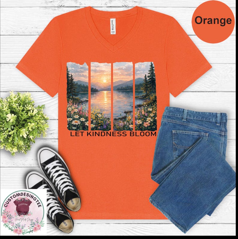 a bright orange t-shirt with a nature-inspired graphic design, including a sunset over a lake and flowers. The t-shirt is accompanied by a pair of blue jeans, a pair of black and white sneakers, and a potted plant.