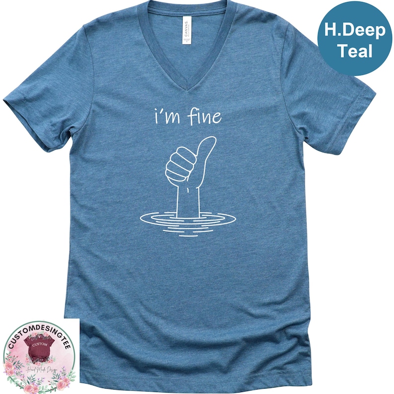 A blue t-shirt with a white graphic design depicting a hand giving a thumbs up, with the text "i'm fine" below the graphic.