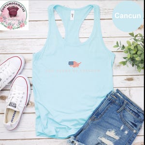 A light blue tank top with the text "250 YEARS OF FREEDOM" printed on it, along with a pair of denim shorts and white sneakers, all laid out on a wooden surface.