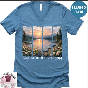 A blue t-shirt with a printed image of a serene landscape depicting a sunset over a lake, surrounded by flowers. The text "LET KINDNESS BLOOM" is printed below the image.