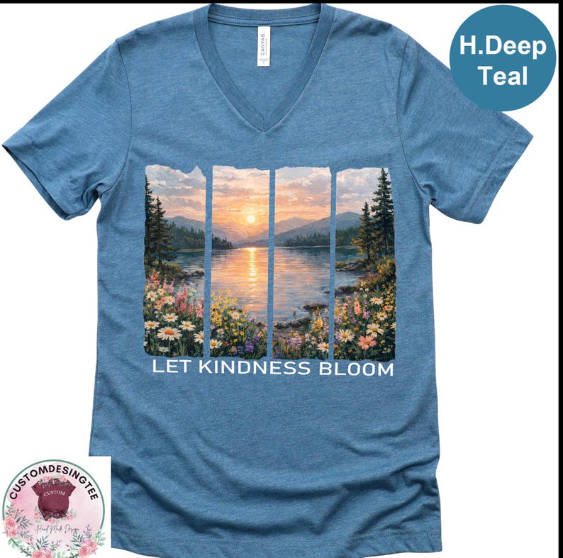 A blue t-shirt with a printed image of a serene landscape depicting a sunset over a lake, surrounded by flowers. The text "LET KINDNESS BLOOM" is printed below the image.