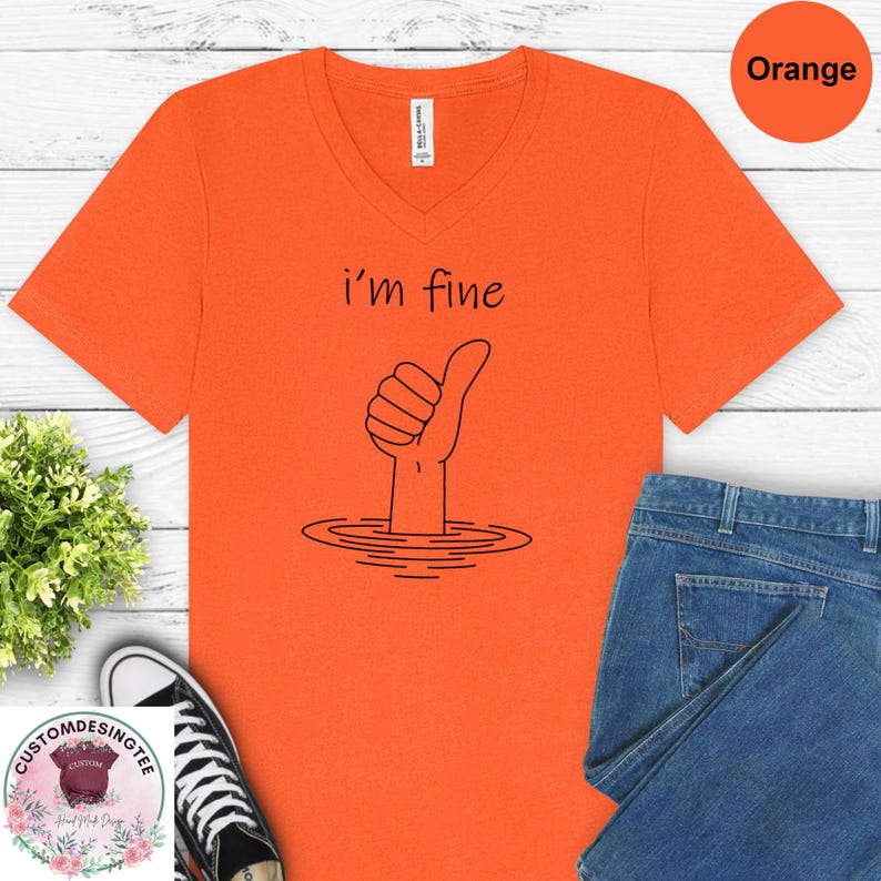 a bright orange t-shirt with a hand-drawn graphic and text, along with a pair of blue jeans and a pair of sneakers, all laid out on a white background.