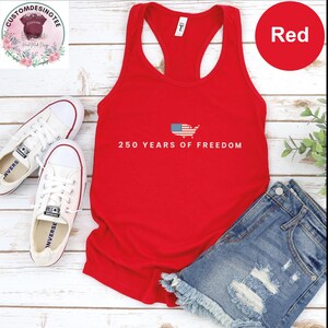 a red tank top, a pair of white sneakers, and a pair of blue denim shorts arranged on a wooden surface.