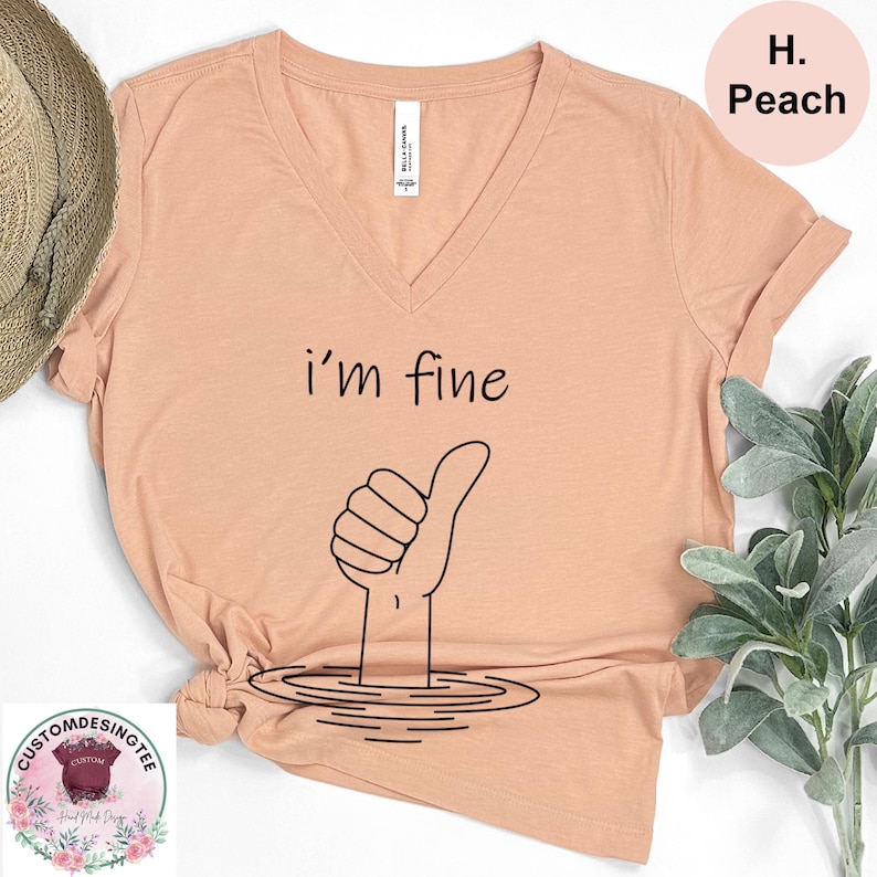 a peach-colored t-shirt with a hand giving a thumbs up, accompanied by a plant and a straw hat.