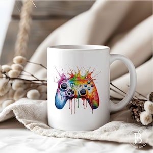 Könnte beinhalten: Weiße Keramiktasse mit einem bunten Farbspritzer-Design einer Videospielkonsole. Der Controller ist regenbogenfarben mit einem schwarz-weißen Design.