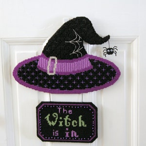 May include: A purple and black witch's hat with a spider hanging from the brim. A sign below reads "The Witch is in".