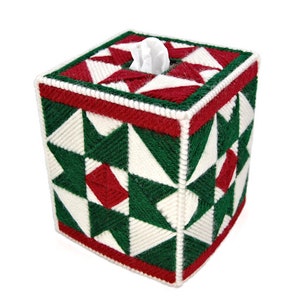 May include: A white, green, and red tissue box cover with a geometric pattern. The cover is made of yarn and has a square shape.