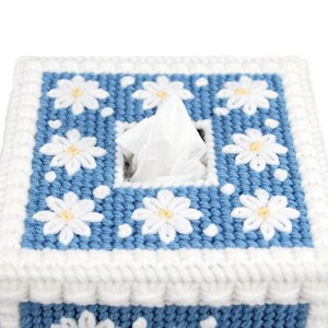 Puede incluir: Una funda para caja de pa&ntilde;uelos de tejido de punto azul y blanco con un pa&ntilde;uelo blanco asomando por la abertura. La funda est&aacute; decorada con margaritas blancas.