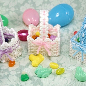 May include: Three small white crocheted baskets with colorful candy inside. The baskets have different colored handles: purple, pink, and blue. The baskets are sitting on a light blue and white floral patterned surface.