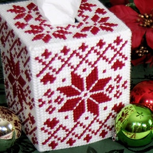 May include: White tissue box cover with a red snowflake pattern. The cover is made of plastic canvas and is decorated with a red snowflake design.