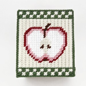 May include: A white and green needlepoint tissue box cover with a red and pink apple design.