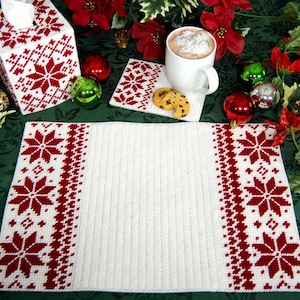 May include: A set of white crocheted placemats with red snowflake designs. The placemats are on a green surface with red poinsettia flowers and ornaments.