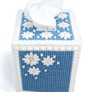 Puede incluir: Una funda para caja de pa&ntilde;uelos de tejido de punto azul y blanco con un patr&oacute;n de margaritas. La funda tiene un borde blanco y una caja de pa&ntilde;uelos blanca en el interior.