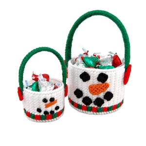 May include: Two white snowman-shaped canvas totes with green handles and red accents. The larger tote is filled with chocolate kisses.