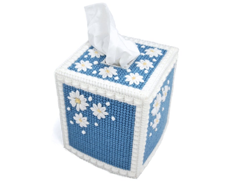 Puede incluir: Una funda para caja de pa&ntilde;uelos azul y blanca con un patr&oacute;n de margaritas. La funda est&aacute; hecha de tela y tiene un borde blanco.