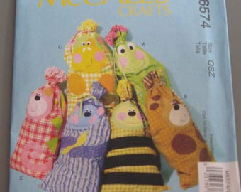 May include: A McCall's Crafts sewing pattern for making five different stuffed toy bags. The bags are shaped like animals and have different patterns and colors. The pattern number is M6574.