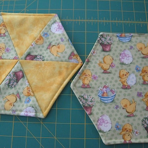 Könnte beinhalten: Zwei gelbe und grüne Stoff-Platzsets mit einem Küken- und Eiermuster. Ein Platzset besteht aus sechs Dreiecken und das andere ist ein Sechseck.