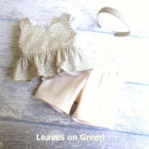 This 3 piece set for your 18 inch doll includes a sleeveless top with peplum ruffle in light moss green with cream leaves all over.  It comes with a pair of cream ribbed knit shorts and a headband covered with the shirt fabric.