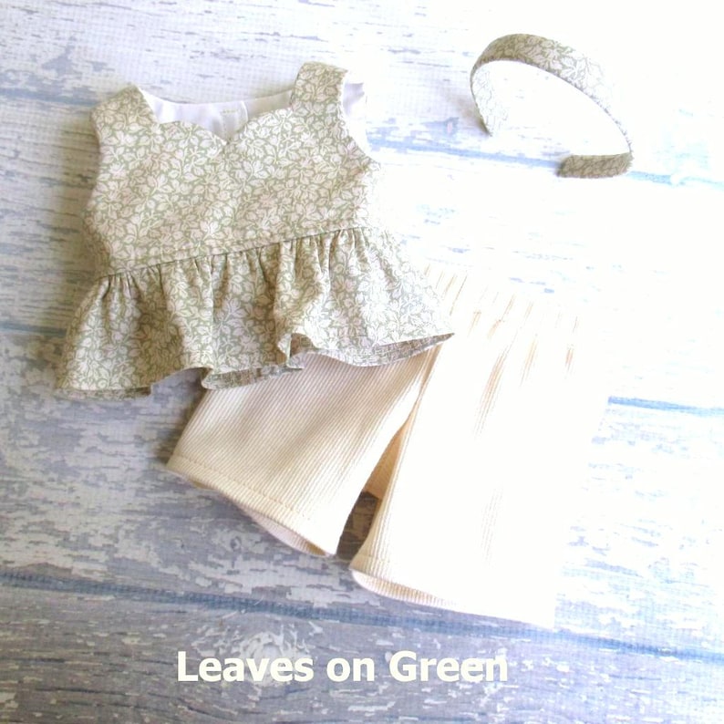 This 3 piece set for your 18 inch doll includes a sleeveless top with peplum ruffle in light moss green with cream leaves all over.  It comes with a pair of cream ribbed knit shorts and a headband covered with the shirt fabric.