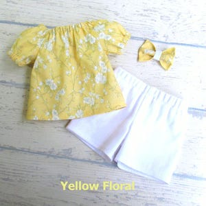 This summer set includes a shirt in light yellow with white and light moss green flowers and leaves; a pair of white stretch knit shorts, and a small hair bow made from the shirt fabric.  Made to fit an 18 inch doll.