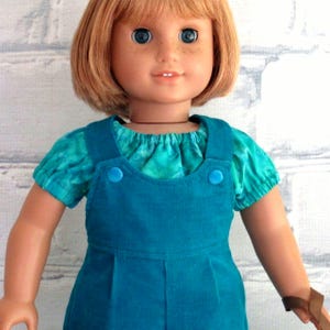 The shirts neckline and sleeves are gathered with elastic, the straps of the overalls snap to the front bib.