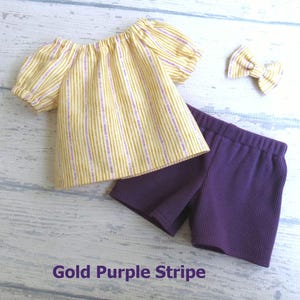 This summer doll outfit includes a shirt made of gold and purple stripes on a cream background; a pair of purple stretch knit shorts, and a hair bow made from the shirt fabric.