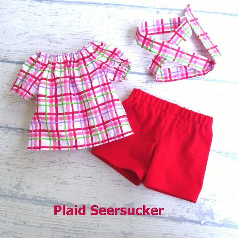 Summer doll outfit includes a seersucker plaid shirt in red, pink, green, and purple plaid on a white background; a pair of red stretch knit shorts; and a hair tie made from the plaid seersucker fabric.