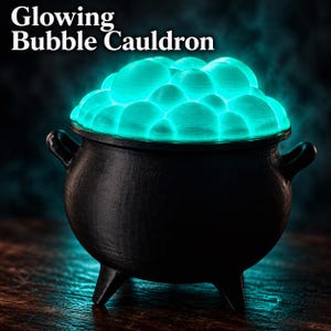 May include: A black three-legged cauldron filled with bright, glowing turquoise bubbles. The text "Glowing Bubble Cauldron" is printed in white at the top. The cauldron has two side handles and a smooth, dark finish, contrasting with the light.