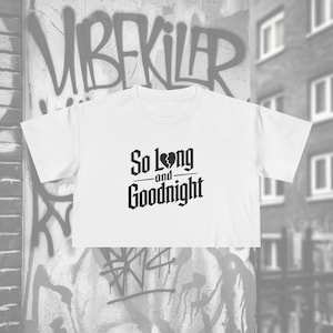 May include: White crop top with the text "So Long and Goodnight" in a gothic font. The shirt has short sleeves and a crew neck. The background features graffiti art.