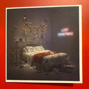 Op de afbeelding: Een vierkante print met een slaapkamer met een bed, kerstversiering en het neonbord "LOST CHRISTMAS". Het bed heeft een rode deken en kussens met hertenpatronen. Een kleine kerstboom staat in de hoek.