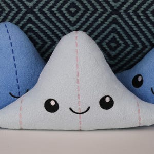 May include: Three plush toys shaped like a cartoon cloud with smiling faces. The clouds are blue and light blue with pink stitching.