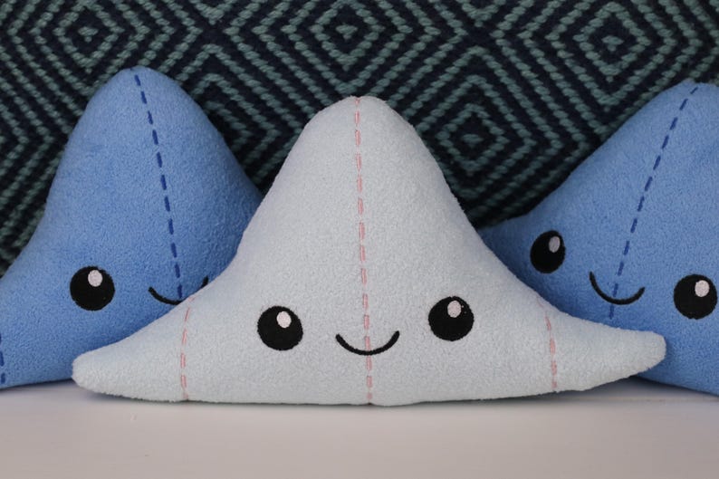 May include: Three plush toys shaped like a cartoon cloud with smiling faces. The clouds are blue and light blue with pink stitching.