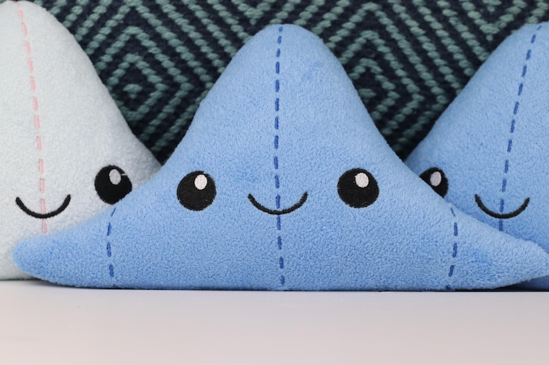 May include: Three plush toys shaped like a cloud with smiling faces. The cloud on the left is light blue with pink stitching, the middle cloud is blue with blue stitching, and the cloud on the right is blue with blue stitching.