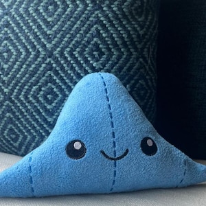 May include: A blue plush toy shaped like a triangle with a smiling face and stitched details.
